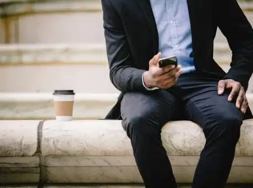 man sitting on bench with coffee on phone