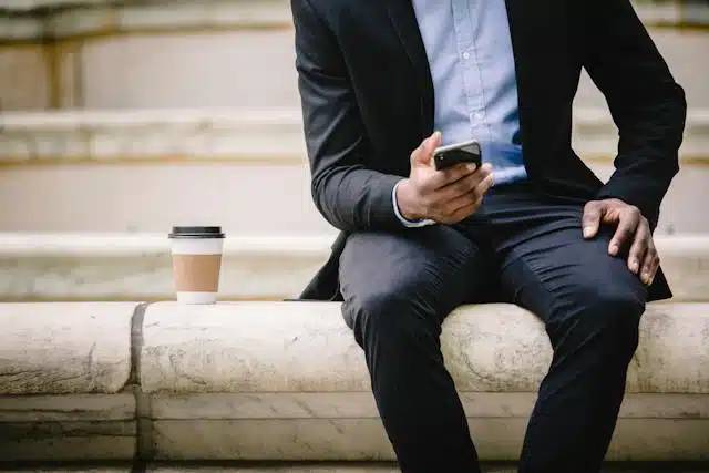 man sitting on bench with coffee on phone