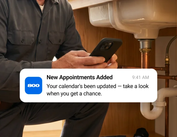 Plumber reviewing an appointment notification beneath a kitchen sink